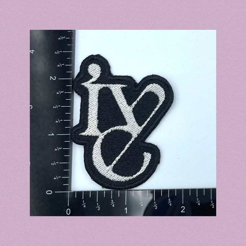 Puede incluir: Un parche bordado en blanco y negro con las letras "IV" en una fuente estilizada.