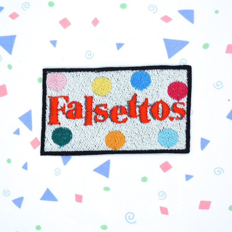 May include: A white embroidered patch with the word "Falseytos" in red lettering and colorful polka dots.