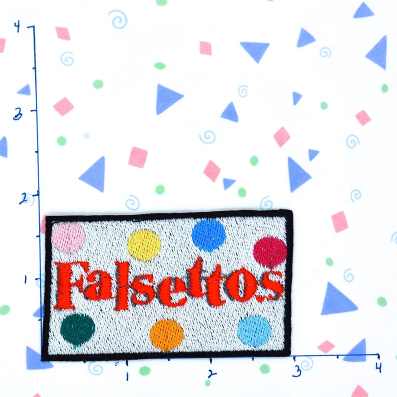 May include: A white embroidered patch with the word "Falsettos" in red lettering and colorful polka dots. The patch has a black border.