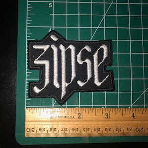 May include: Black embroidered patch with the word "zipse" in white lettering.