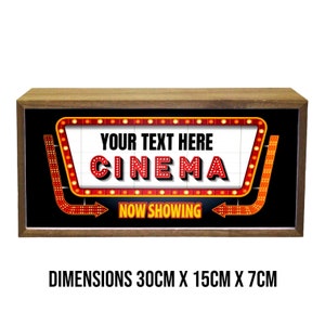 Puede incluir: Una caja de luz con marco de madera con fondo negro y un letrero de marquesina rojo y amarillo que dice "YOUR TEXT HERE CINEMA NOW SHOWING". El letrero mide 30 cm de ancho, 15 cm de alto y 7 cm de profundidad.