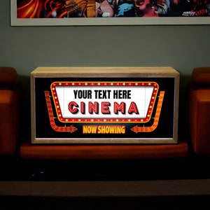Puede incluir: Un letrero de madera con un marquesina roja y blanca que dice "YOUR TEXT HERE CINEMA" y "NOW SHOWING". El letrero est&aacute; iluminado con luces amarillas.