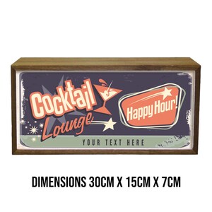 Pu&ograve; includere: Un cartello in legno in stile retr&ograve; con sfondo blu e una grafica di un bicchiere da cocktail rosso e bianco. Il cartello dice "Cocktail Lounge" e "Happy Hour!" in un font vintage. Il cartello misura 30 cm x 15 cm x 7 cm.