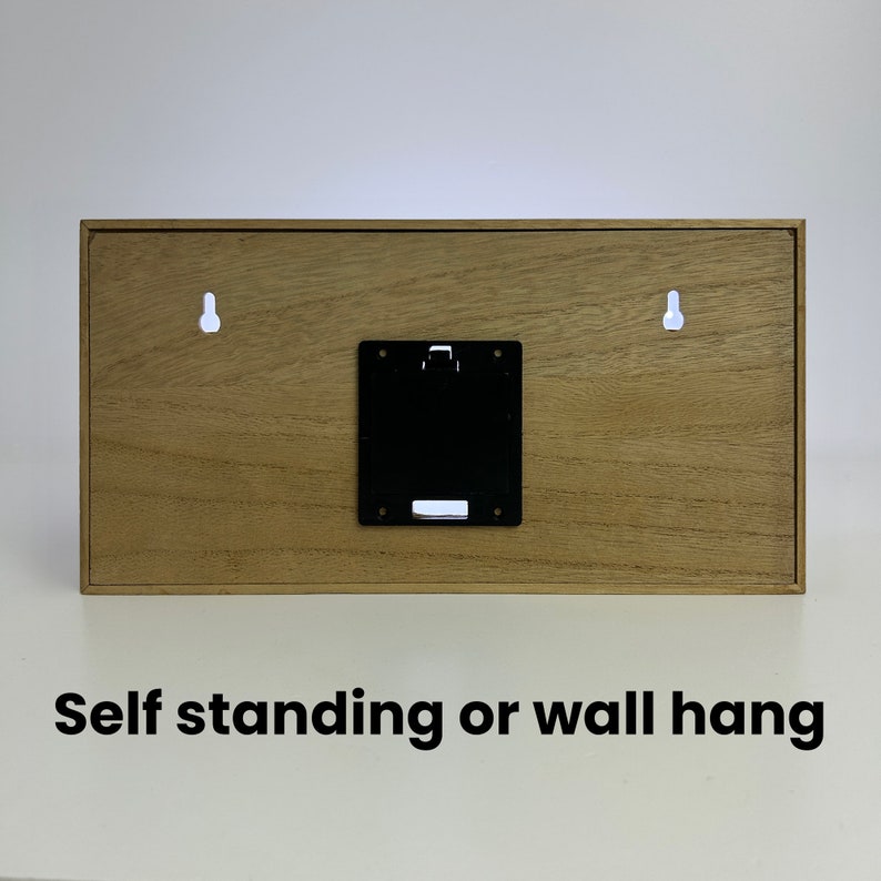 Puede incluir: La parte posterior de un letrero de madera con dos agujeros para colgar y un compartimento para bater&iacute;as negro. El letrero dice "Self standing or wall hang".
