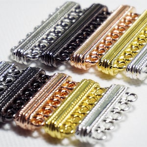 May include: An assortment of multi-strand jewelry clasps in various metallic finishes. The clasps are silver, black, copper, gold, and silver. Each clasp has a decorative filigree design and multiple loops for attaching jewelry strands.