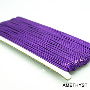Pode incluir: Um close-up de um carretel de cord&atilde;o el&aacute;stico roxo ametista. O cord&atilde;o est&aacute; enrolado firmemente e pronto para ser usado em projetos de artesanato.
