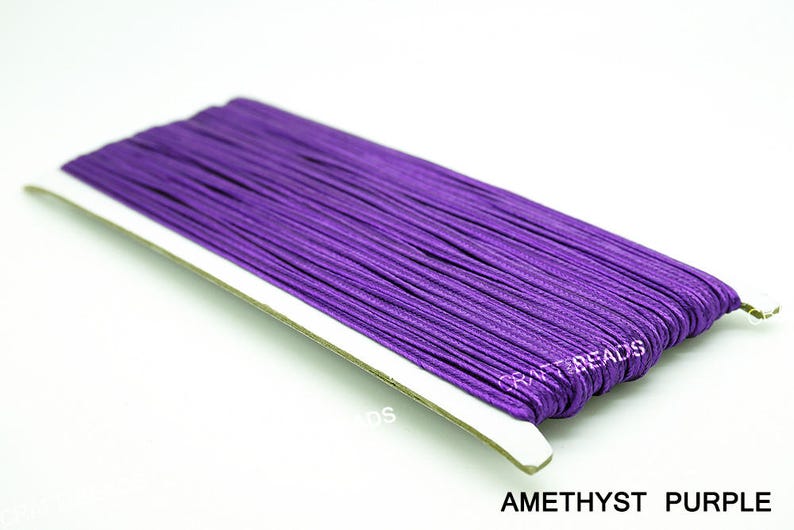 Pode incluir: Um close-up de um carretel de cord&atilde;o el&aacute;stico roxo ametista. O cord&atilde;o est&aacute; enrolado firmemente e pronto para ser usado em projetos de artesanato.