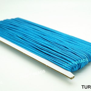 Pode incluir: Um carretel de cord&atilde;o azul turquesa, enrolado em um suporte de cart&atilde;o branco. O suporte tem o texto "CRAFT BEADS" impresso nele. O texto "TURQUOISE" est&aacute; impresso abaixo do carretel.