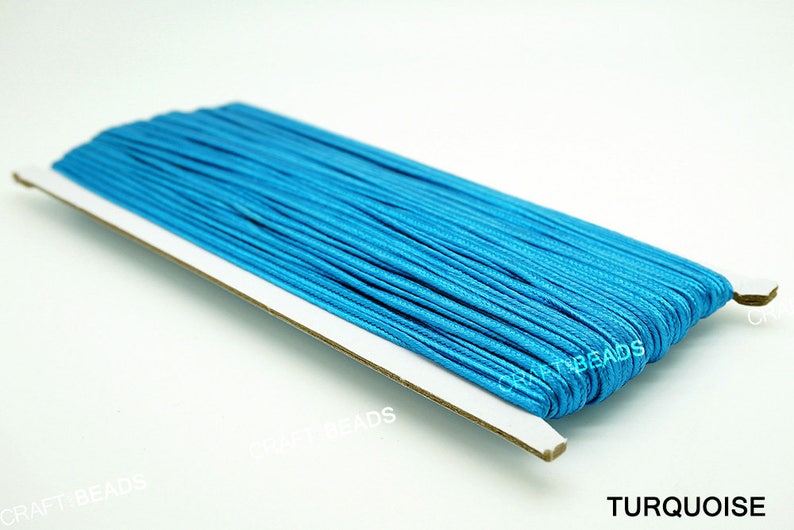 Pode incluir: Um carretel de cord&atilde;o azul turquesa, enrolado em um suporte de cart&atilde;o branco. O suporte tem o texto "CRAFT BEADS" impresso nele. O texto "TURQUOISE" est&aacute; impresso abaixo do carretel.