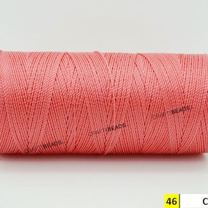 May include: A spool of coral colored thread. The spool is labeled "46 Coral".