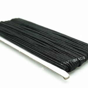 Pode incluir: Um carretel de cord&atilde;o el&aacute;stico preto, enrolado firmemente em um suporte de cart&atilde;o branco. O r&oacute;tulo no suporte diz "CRAFTBEADS".