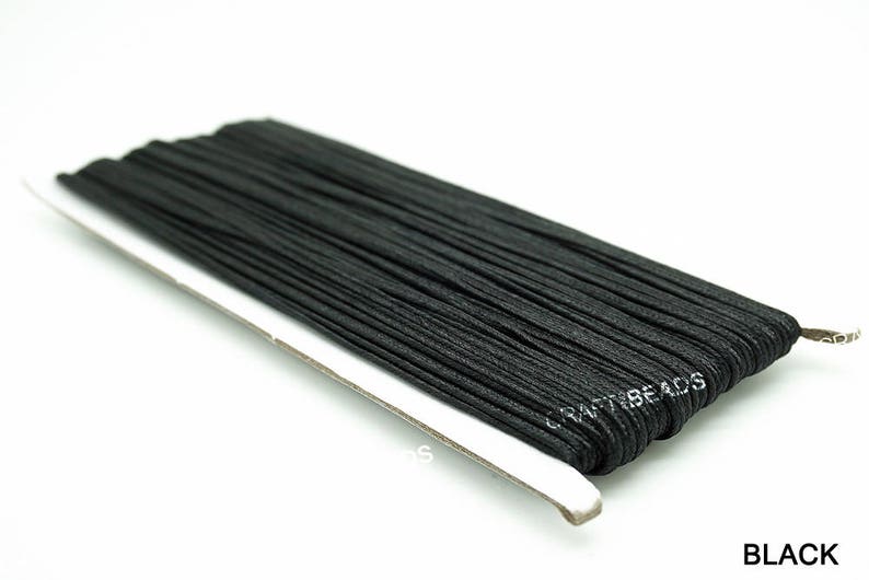 Pode incluir: Um carretel de cord&atilde;o el&aacute;stico preto, enrolado firmemente em um suporte de cart&atilde;o branco. O r&oacute;tulo no suporte diz "CRAFTBEADS".