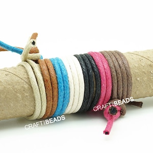 May include: A collection of 10 different colored waxed cotton cords wrapped around a cardboard tube. The cords are all 1 mm thick and are available in a variety of colors, including white, black, brown, blue, and pink. The cords are labeled "CRAFT BEADS".