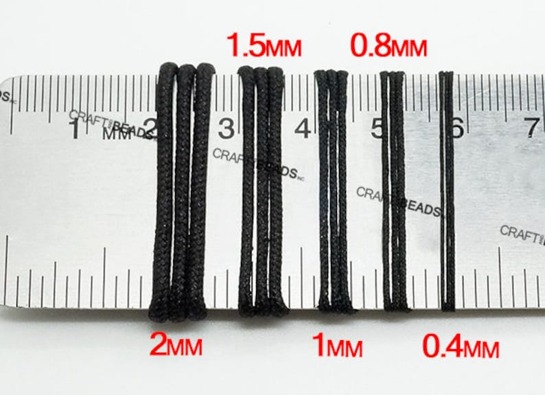 May include: Close-up of four black elastic cords of different thicknesses measured against a ruler. The cords are labeled with their measurements in millimeters: 2mm, 1.5mm, 1mm, and 0.4mm.
