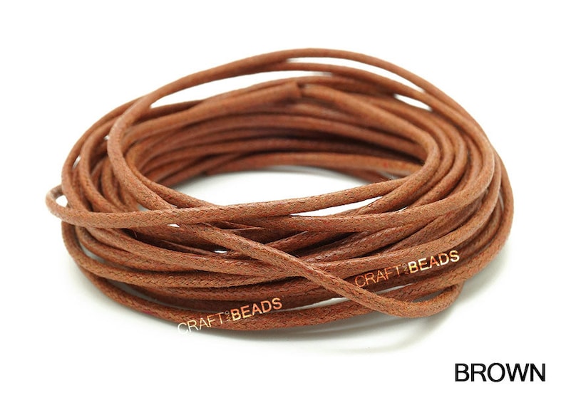 May include: A spool of brown leather cord, approximately 1.5 mm thick, for crafting and jewelry making. The cord is wound tightly and has a smooth, textured surface. The text "CRAFT BEADS" is printed on the cord.