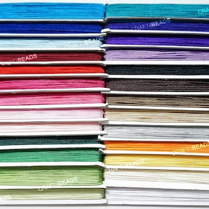 May include: A collection of 18 spools of colourful elastic cord, each wound neatly and labelled with the text "CRAFT BEADS". The cords are arranged in rows, showcasing a variety of vibrant hues, including blue, purple, red, pink, white, green, orange, yellow, and beige.