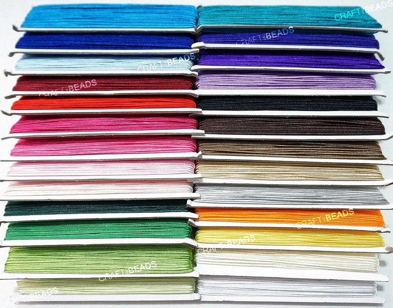 Pode incluir: Uma cole&ccedil;&atilde;o de 18 carret&eacute;is de cord&atilde;o el&aacute;stico colorido, cada um enrolado cuidadosamente e etiquetado com o texto "CRAFT BEADS". Os cord&otilde;es est&atilde;o dispostos em filas, mostrando uma variedade de tons vibrantes, incluindo azul, roxo, vermelho, rosa, branco, verde, laranja, amarelo e bege.