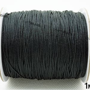 May include: A spool of black 1 mm waxed cord. The cord is wound tightly around a white cardboard spool.