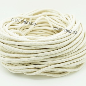 May include: A close-up of a large spool of natural white cotton cord. The cord is tightly wound and appears to be soft and pliable.