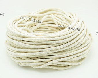 Puede incluir: Primer plano de un carrete grande de cordón de algodón blanco natural. El cordón está enrollado apretado y parece suave y flexible.