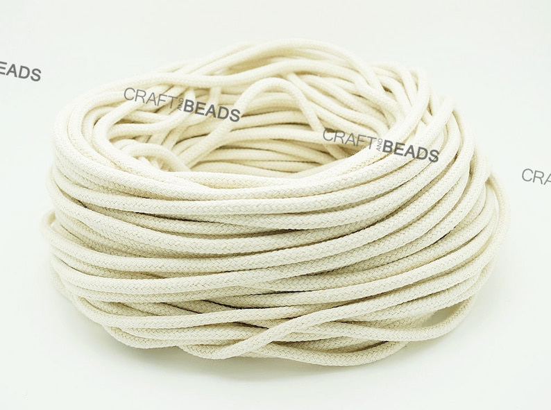 May include: A close-up of a large spool of natural white cotton cord. The cord is tightly wound and appears to be soft and pliable.