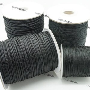 May include: Four spools of black waxed cotton cord, each wound on a white cardboard spool with the text "CRAFTIBEADS" printed on the side.