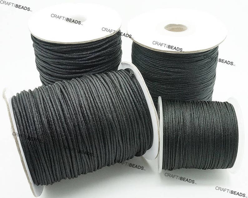 May include: Four spools of black waxed cotton cord, each wound on a white cardboard spool with the text "CRAFTIBEADS" printed on the side.