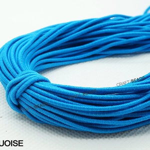 K&ouml;nnte beinhalten: Nahaufnahme eines t&uuml;rkisfarbenen Gummibandes, das zu einer Spirale gewickelt ist. Das Band ist glatt und hat einen leichten Glanz. Der Text "CRAFT BEADS" ist auf dem Band sichtbar. Das Wort "TURQUOISE" ist in wei&szlig;en Buchstaben unter dem Band gedruckt.
