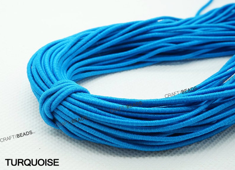 K&ouml;nnte beinhalten: Nahaufnahme eines t&uuml;rkisfarbenen Gummibandes, das zu einer Spirale gewickelt ist. Das Band ist glatt und hat einen leichten Glanz. Der Text "CRAFT BEADS" ist auf dem Band sichtbar. Das Wort "TURQUOISE" ist in wei&szlig;en Buchstaben unter dem Band gedruckt.
