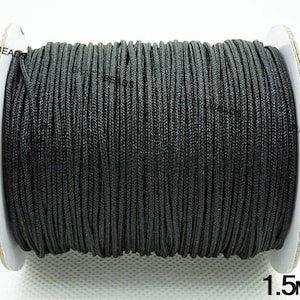 May include: A spool of black cord with a 1.5 mm diameter. The cord is wound tightly around the spool, which is made of white cardboard.