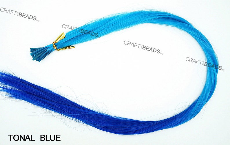 Puede incluir: Una hebra de extensiones de cabello azul con un degradado de azul claro a azul oscuro. Las extensiones de cabello est&aacute;n sujetas a un peque&ntilde;o clip dorado.
