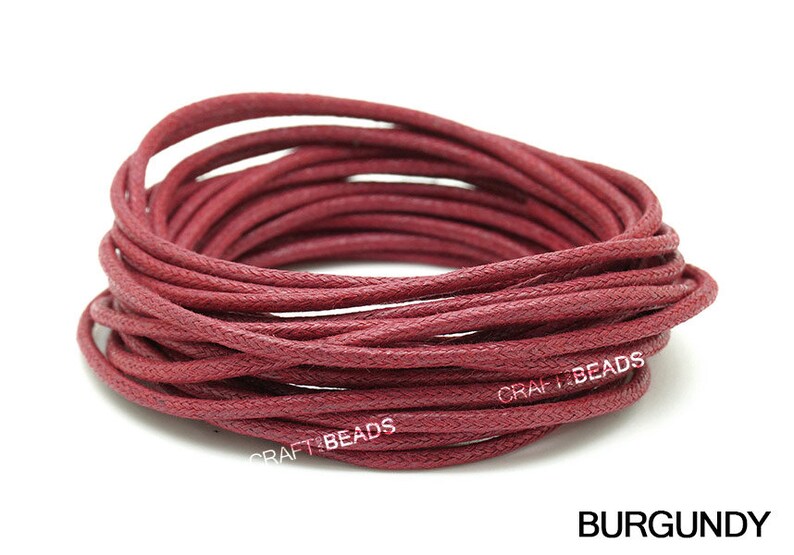 May include: A close-up of a spool of burgundy waxed cotton cord. The cord is tightly wound and has a textured surface. The text "CRAFT BEADS" is visible on the spool.
