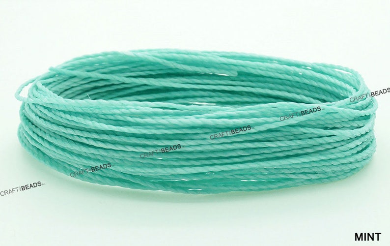 K&ouml;nnte beinhalten: Nahaufnahme einer Spule mit mintgr&uuml;nem gewachstem Baumwollgarn. Das Garn ist gedreht und hat einen dezenten Glanz. Die Spule ist mit "CRAFT BEADS." beschriftet.