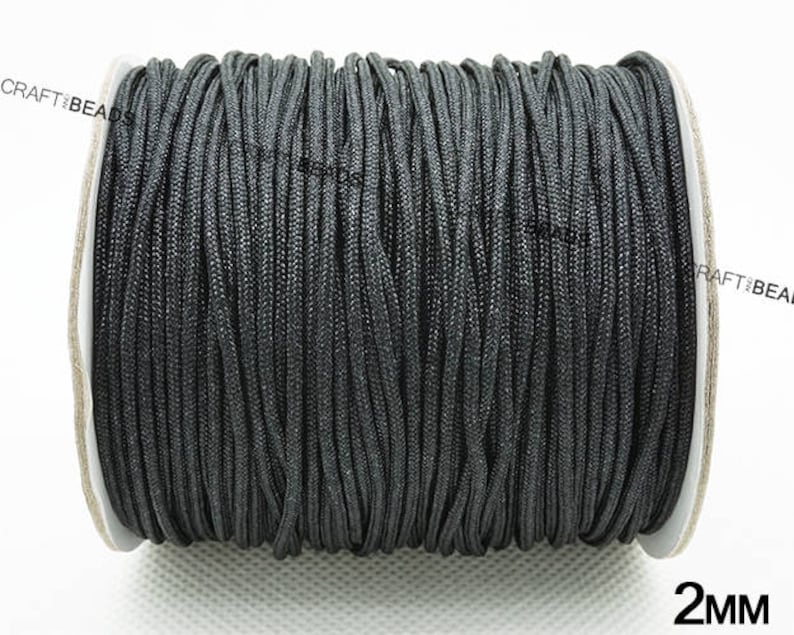 May include: A spool of black 2mm cord. The cord is wound tightly around the spool, which is made of white cardboard. The spool is labeled with the text "CRAFTIBEADS" and "2MM".