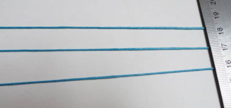 May include: Three strands of light blue cord or string are laid out horizontally on a white surface. A ruler is visible on the right side of the image, with the numbers 16, 17, 18, 19, and 20 visible.