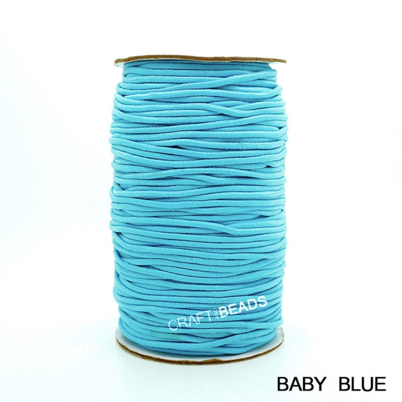 May include: A spool of light blue elastic cord, wound around a cardboard tube. The label on the tube reads "CRAFT BEADS". The text "BABY BLUE" is printed below the image.