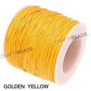 May include: A spool of golden yellow waxed cotton cord. The cord is wound tightly around a white plastic spool. The spool is labeled "CRAFT and BEADS INC."