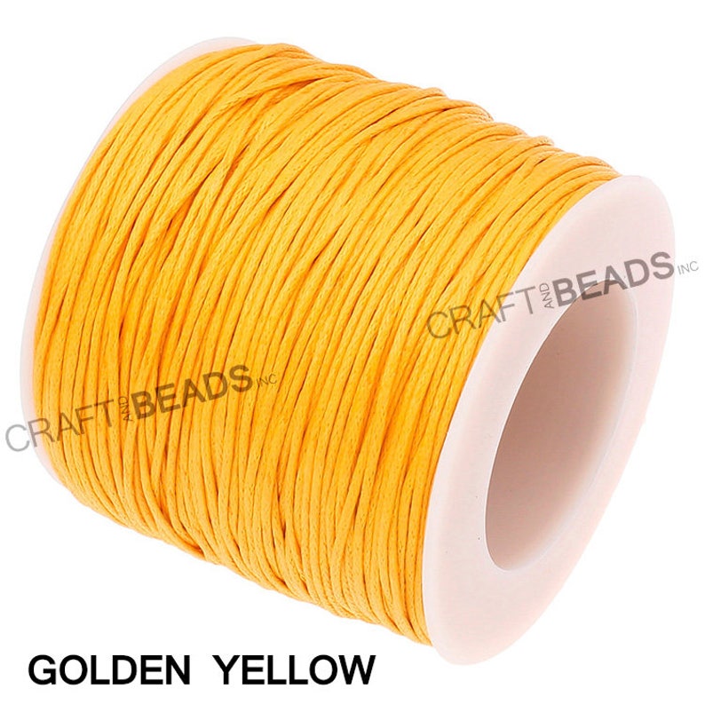 May include: A spool of golden yellow waxed cotton cord. The cord is wound tightly around a white plastic spool. The spool is labeled "CRAFT and BEADS INC."