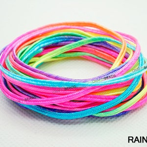 Pode incluir: Um close-up de um conjunto de cord&otilde;es coloridos do arco-&iacute;ris. Os cord&otilde;es s&atilde;o feitos de um material macio e flex&iacute;vel e t&ecirc;m um brilho sutil. Os cord&otilde;es s&atilde;o dispostos em um padr&atilde;o circular, com as pontas dos cord&otilde;es sobrepostas. Os cord&otilde;es s&atilde;o etiquetados com "CRAFT BEADS" no canto inferior esquerdo da imagem. O texto "RAINBOW" est&aacute; no canto inferior direito da imagem.