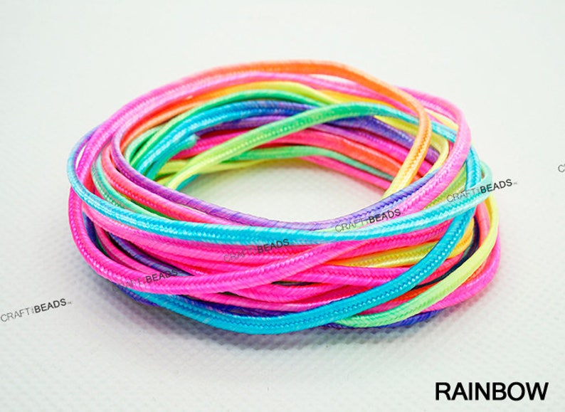 Pode incluir: Um close-up de um conjunto de cord&otilde;es coloridos do arco-&iacute;ris. Os cord&otilde;es s&atilde;o feitos de um material macio e flex&iacute;vel e t&ecirc;m um brilho sutil. Os cord&otilde;es s&atilde;o dispostos em um padr&atilde;o circular, com as pontas dos cord&otilde;es sobrepostas. Os cord&otilde;es s&atilde;o etiquetados com "CRAFT BEADS" no canto inferior esquerdo da imagem. O texto "RAINBOW" est&aacute; no canto inferior direito da imagem.