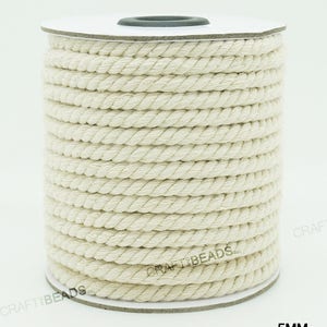 Pu&ograve; includere: Un rotolo di corda di cotone bianco naturale, di 5 mm di spessore, su un rotolo di cartone bianco. La corda &egrave; avvolta strettamente e ha una texture naturale leggermente ruvida. Il rotolo &egrave; etichettato con "CRAFT BEADS INC" e "5MM".