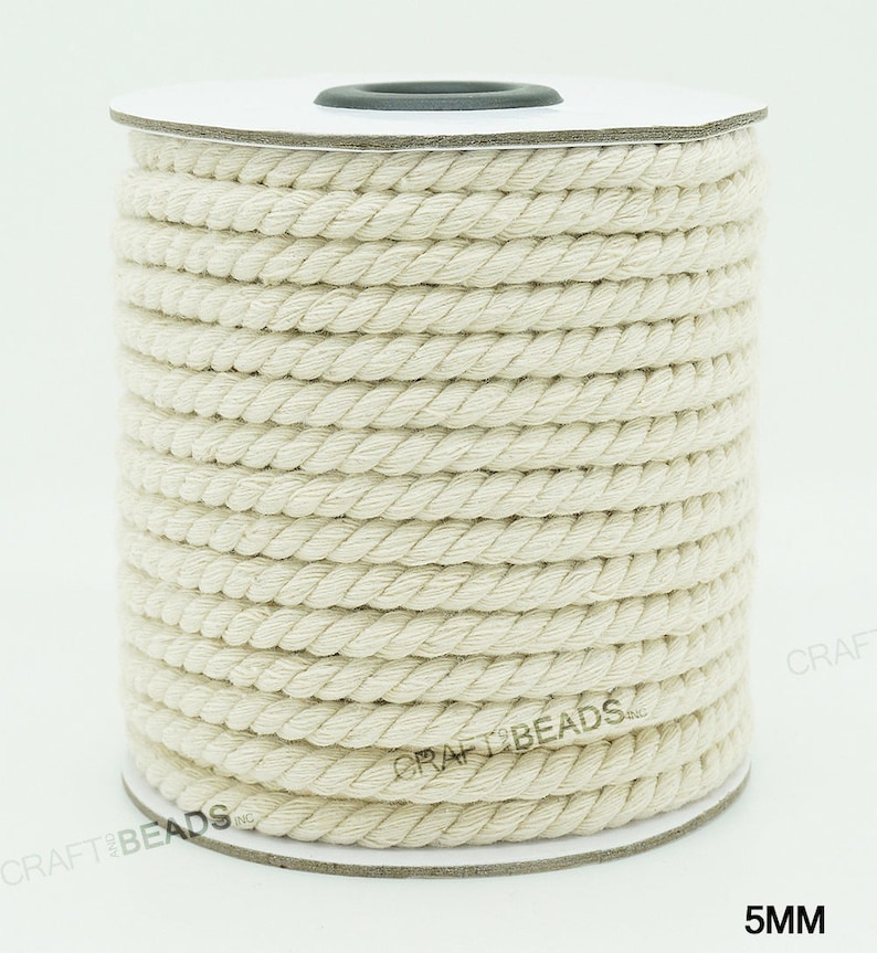 Pu&ograve; includere: Un rotolo di corda di cotone bianco naturale, di 5 mm di spessore, su un rotolo di cartone bianco. La corda &egrave; avvolta strettamente e ha una texture naturale leggermente ruvida. Il rotolo &egrave; etichettato con "CRAFT BEADS INC" e "5MM".