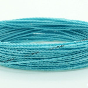 K&ouml;nnte beinhalten: Nahaufnahme einer Spule mit hellblauem gewachstem Garn. Das Garn ist gedreht und hat eine glatte Textur. Der Text "CRAFT BEADS" ist auf der Spule sichtbar.