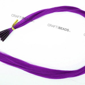 Puede incluir: Una hebra de extensiones de cabello sint&eacute;tico largo y de color morado brillante con un clip dorado en la parte superior. El cabello es liso y recto, y el clip est&aacute; unido a un paquete de hebras de cabello. El texto "PURPLE" est&aacute; impreso en blanco en la parte inferior de la imagen.
