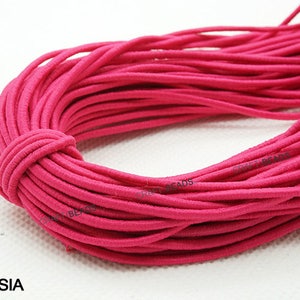 K&ouml;nnte beinhalten: Nahaufnahme einer Spule mit fuchsiafarbenem Gummiband. Das Band ist fest gewickelt und wirkt weich und dehnbar.
