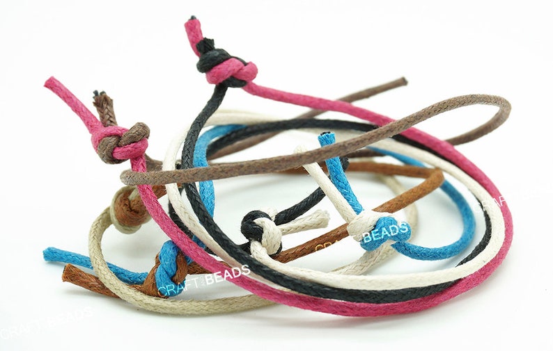 May include: Assortment of colorful cotton cords in various colors, including brown, black, white, pink, and blue. The cords are knotted and arranged in a circular pattern.  CRAFT BEADS is visible on the cords.