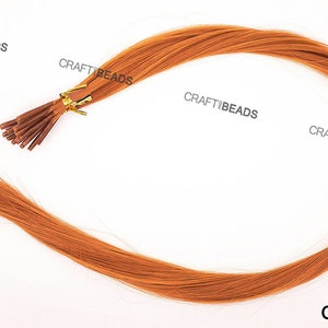 Puede incluir: Una hebra de extensiones de cabello humano de color caramelo con microanillos unidos. El cabello es liso y parece tener unos 45 cm de largo.