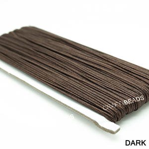 Pode incluir: Um carretel de cord&atilde;o encerado marrom escuro, perfeito para fazer joias, artesanato e projetos de macram&ecirc;. O cord&atilde;o est&aacute; enrolado em torno de um cart&atilde;o branco com o texto "CRAFT BEADS" impresso nele. O texto "DARK BROWN" est&aacute; impresso abaixo do carretel.
