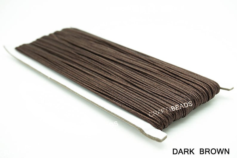 Pode incluir: Um carretel de cord&atilde;o encerado marrom escuro, perfeito para fazer joias, artesanato e projetos de macram&ecirc;. O cord&atilde;o est&aacute; enrolado em torno de um cart&atilde;o branco com o texto "CRAFT BEADS" impresso nele. O texto "DARK BROWN" est&aacute; impresso abaixo do carretel.
