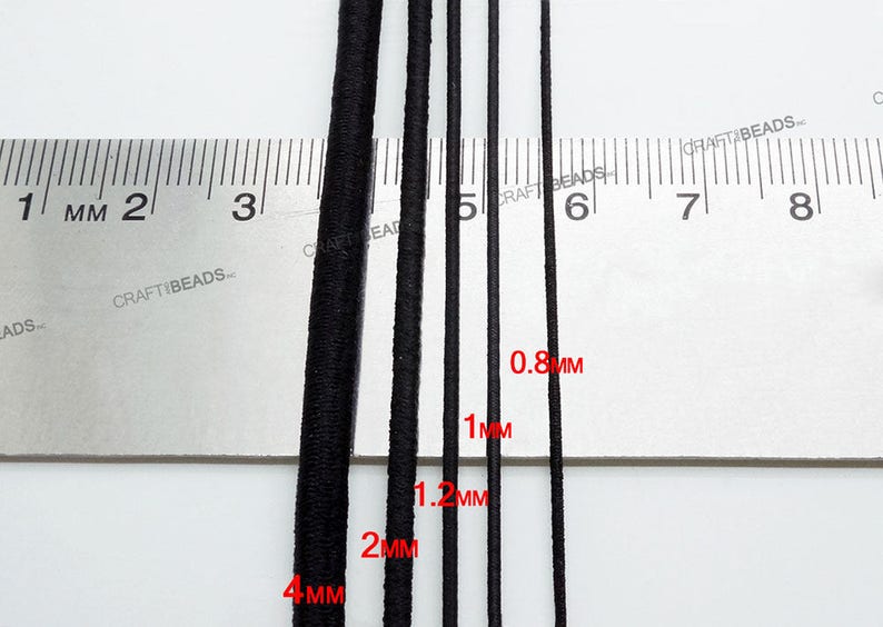 K&ouml;nnte beinhalten: F&uuml;nf schwarze Gummib&auml;nder in verschiedenen St&auml;rken, gemessen in Millimetern, auf einem wei&szlig;en Lineal. Die B&auml;nder haben einen Durchmesser von 0,8 mm, 1 mm, 1,2 mm, 2 mm und 4 mm.